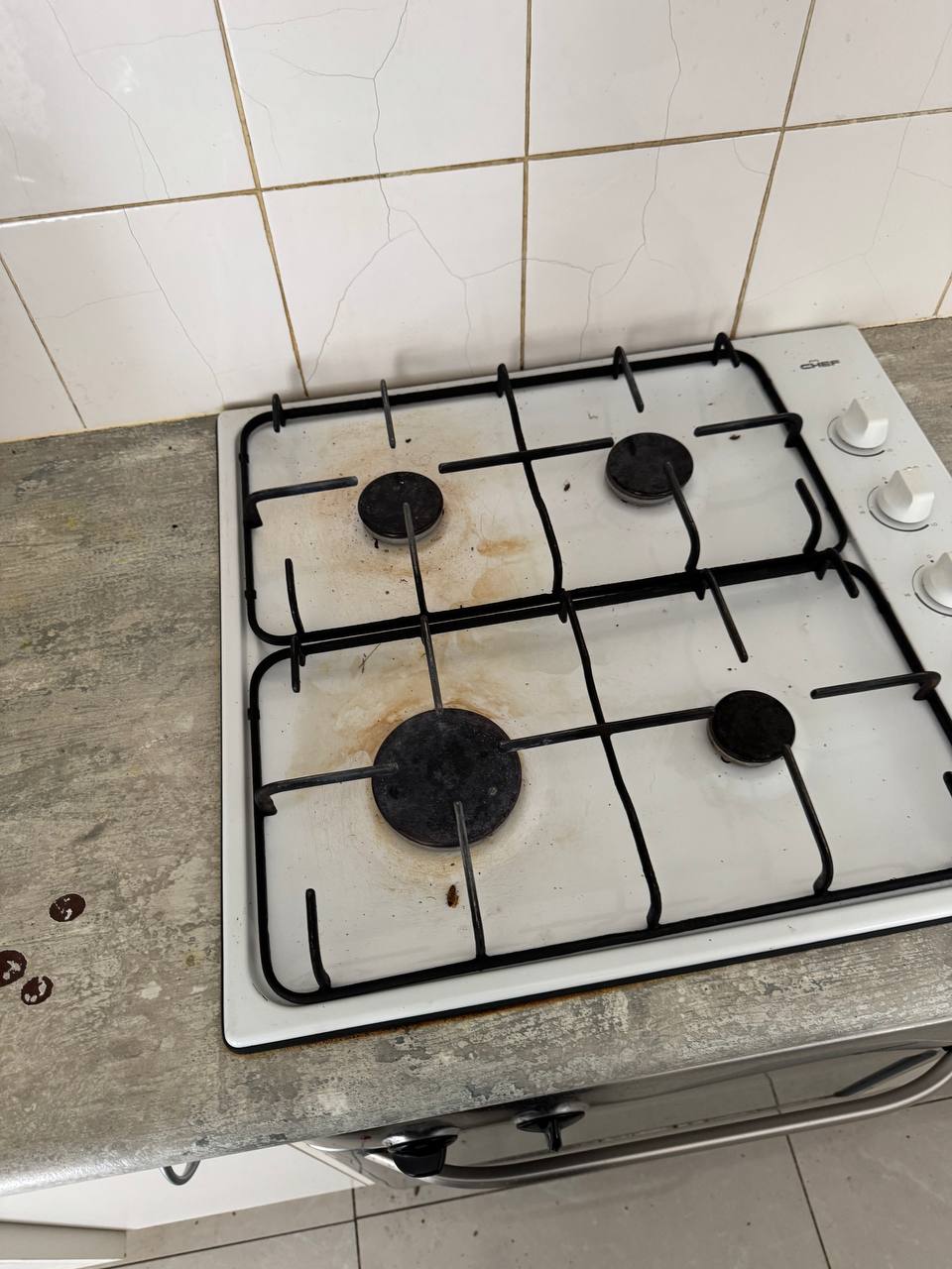 Dirty gas cooktop with burnt food residue and grease buildup before professional cleaning — before